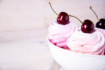 Lots of sweet pink cherry cakes in a white plate on a wooden background. Pink cherry marshmallows.