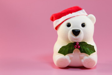 Toy - white bear with Santa's hat. He holds in his paws a twig with green leaves and berries. Background - gently pink.