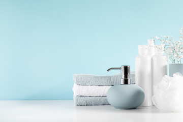 Fototapeta na wymiar Soft light bathroom decor in pastel blue color, towel, soap dispenser, white flowers, accessories on white wood shelf. Elegant decor bathroom interior.