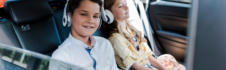 panoramic shot of boy listening music in headphones near sister in car © LIGHTFIELD STUDIOS