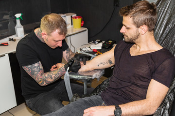 Professional tattooer doing picture on hand of man