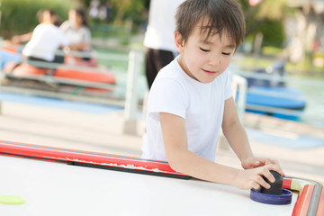 Joyful asian child boy playing air hockey outdoors. Family sporting events in the park.
