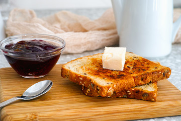 Two toasts with piece of butter on wooden board and  bowl with jam.
