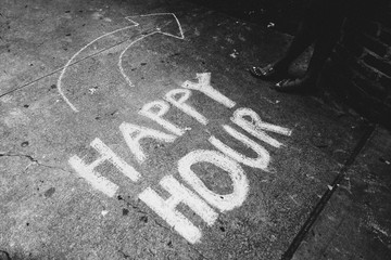 Happy hour written in chalk on sidewalk