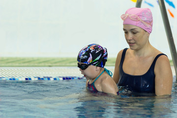 Mother teaching little girl to swim in the swimming pool