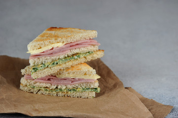 Sandwiches of white bread on Kraft paper. Sandwich stuffing consists of ham, cheese and scrambled eggs with spinach. Close-up.