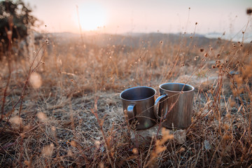 Two metal cups of tea among the grass against the backdrop of the mountains. Concept of autumn hiking trips
