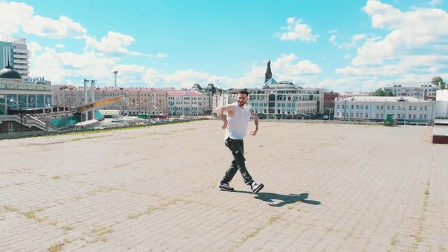 A young attractive tattooed man dancing on the roof on the background of the city center