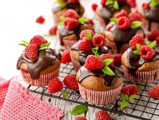 Raspberry cupcakes with melted dark chocolate, fresh raspberries and mint on a cooling tray on a white table, close up.  A delicious dessert or breakfast