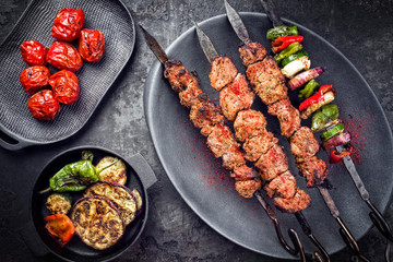 Traditional Russian shashlik on a barbecue skewer with vegetable and sumach paste as top view on a modern design plate