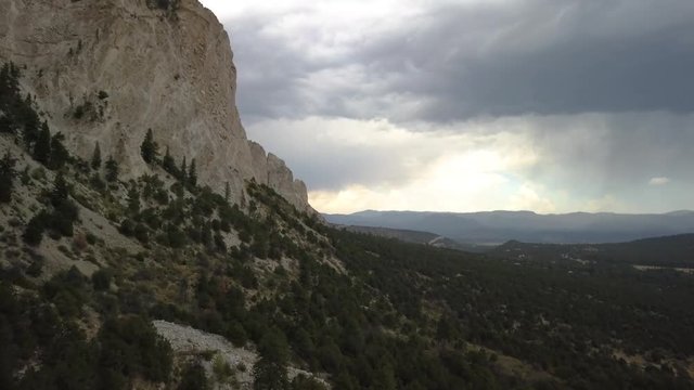 Aerial shot flying next to a large rocky cliff with dark stormy clouds on the horizon