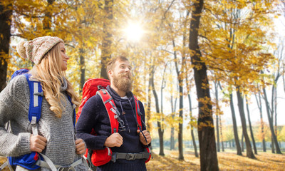 Fototapeta na wymiar adventure, travel, tourism, hike and people concept - couple of travelers with backpacks over autumn park background