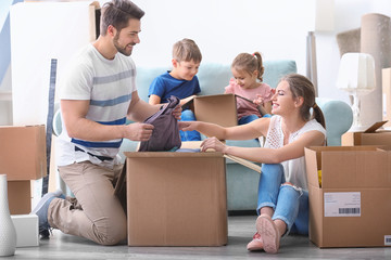 Young couple packing boxes with their children indoors. Happy family on moving day