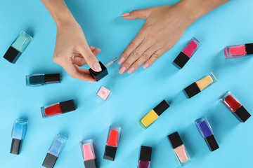 Woman applying nail polish on color background, above view