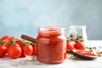 Composition with jar of tasty tomato sauce on table against color background