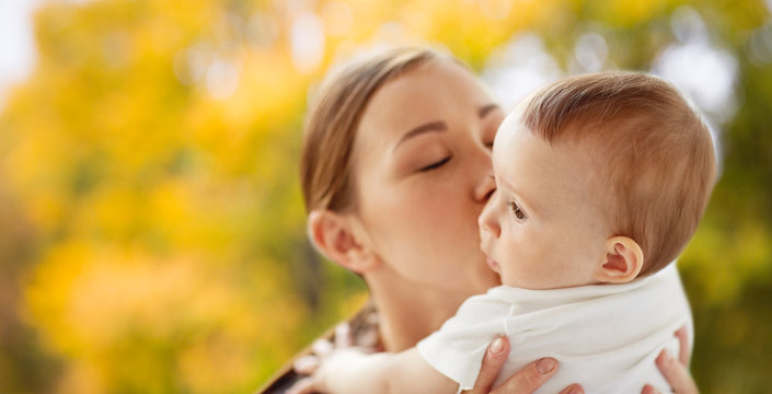 family, child and parenthood concept - close up of happy smiling young mother kissing little baby over autumn background