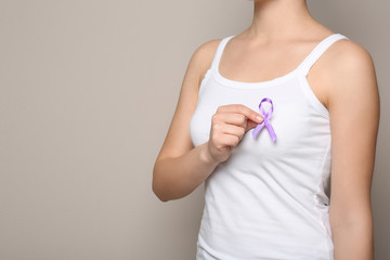 Woman holding purple ribbon on grey background, closeup with space for text. Domestic violence...