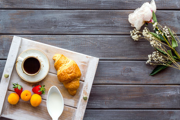 croissant with fruit, and coffee with cream for homemade breakfast on the tray on wooden background top view