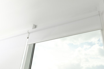 Modern window with white roller blinds indoors, low angle view