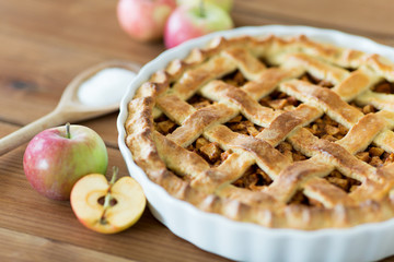 food, culinary and baking concept - close up of apple pie with cinnamon and sugar on wooden table