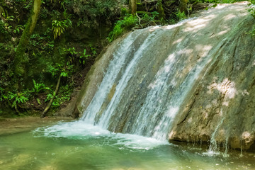 View of the mountain waterfall in the province of Veneto, Italy. Falling stream of water among rocks and green forest.