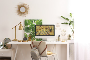 Modern workplace with computer and golden decor on desk near wall. Stylish interior design