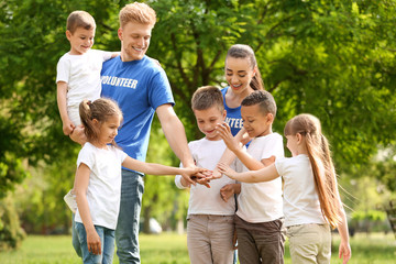 Group of kids joining hands with volunteers in park