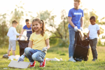 Little girl collecting trash in park. Volunteer project
