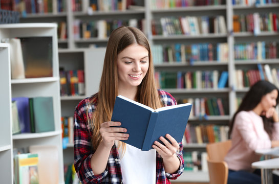 Young pretty woman reading book in library