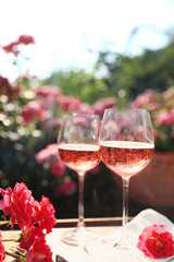Glasses of rose wine on table in blooming garden