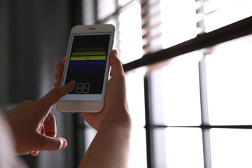 Woman using smart home application on phone to control window blinds indoors, closeup. Space for text