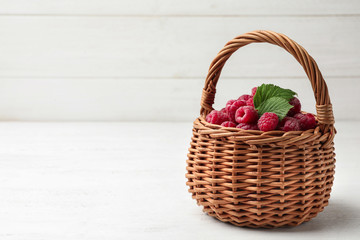Fototapeta na wymiar Basket of delicious fresh ripe raspberries with leaves on white wooden table, space for text