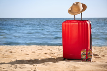 Bright suitcase, hat and flip flops on sand near sea, space for text. Beach accessories