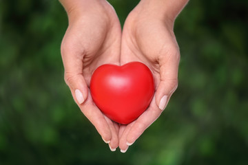 Young woman holding red heart on blurred green background, closeup. Donation concept
