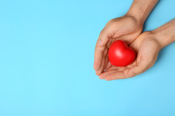 Young man holding red heart on light blue background, top view with space for text. Donation concept