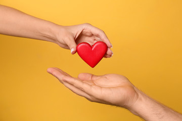 Woman giving red heart to man on yellow background, closeup. Donation concept - obrazy, fototapety, plakaty