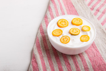 greek yogurt with kumquat pieces in a white plate on a white wooden background