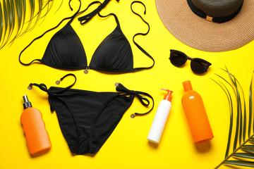 Flat lay composition with black swimsuit and beach accessories on yellow background
