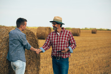 Naklejka na ściany i meble farmer shaking hands with his young colleague in wheat field