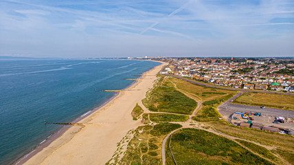 A beautiful aerial  seaside view with sandy beach, crystal blue water, groynes (breakwaters), green vegetation dunes and parking along a town under a majestic blue sky and white clouds