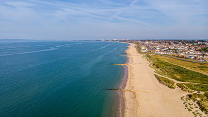 A beautiful aerial  seaside view with sandy beach, crystal blue water, groynes (breakwaters) and green vegetation dunes along a town under a majestic blue sky and white clouds