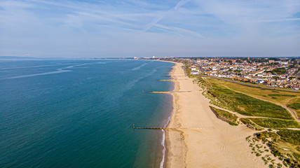 A beautiful aerial  seaside view with sandy beach, crystal blue water, groynes (breakwaters) and green vegetation dunes along a town under a majestic blue sky and white clouds