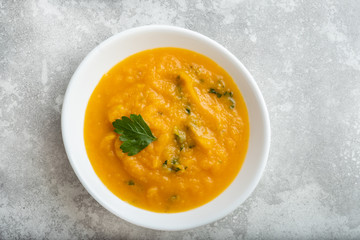 Roasted pumpkin and carrot soup with cream and pumpkin seeds on white wooden background. Copy space