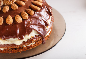 Homemade chocolate cake with milk cream, caramel and almonds on white wooden background.