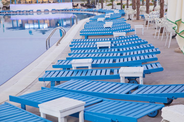 Lounge sunbeds near swimming pool .Sun loungers by the pool, blue, comfortable atmosphere .Swimming pool beds in nature. Empty sunbeds by the beautiful resort pool .