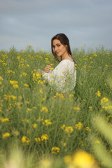 Fototapeta premium Beautiful woman on yellow flowers field with dark cloudy sky