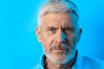 portrait of a frowning gray-haired man with a beard on blue background