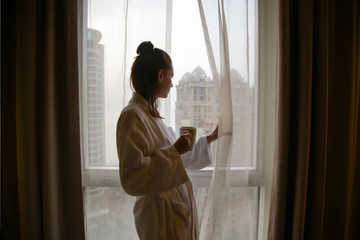 Woman drinking the first-morning coffee next to the window 