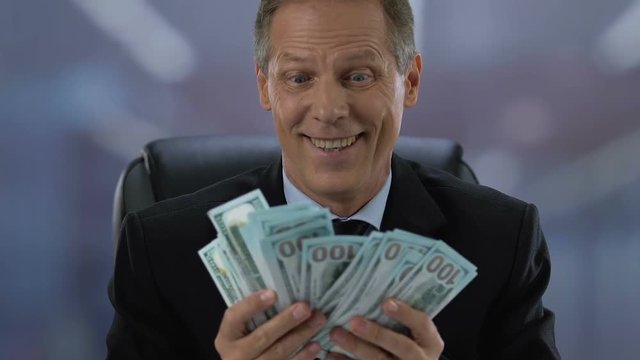 Excited mature businessman holding dollar banknotes in hands, company income