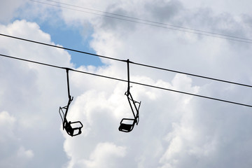 2 hanging chairs at old single seat chair lift against cloudy sky